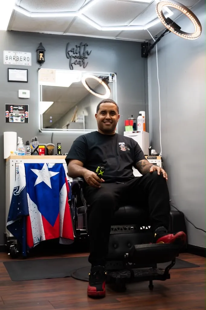 Milton Leyro, barber and owner, seated in his chair at Jireh Dios Proveerá Barbershop